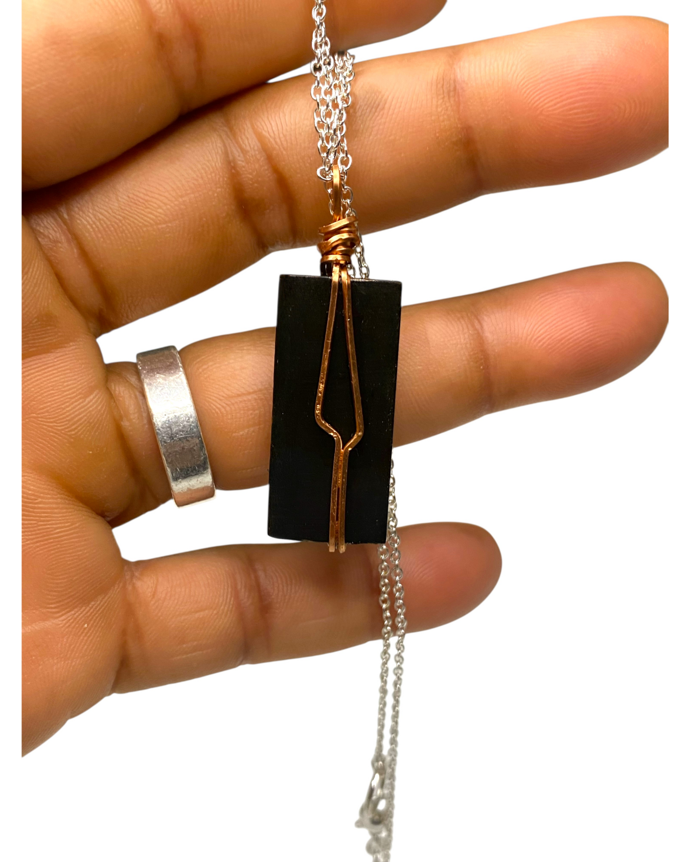 Hand holding a necklace with a black pendant and copper wire design on a white background