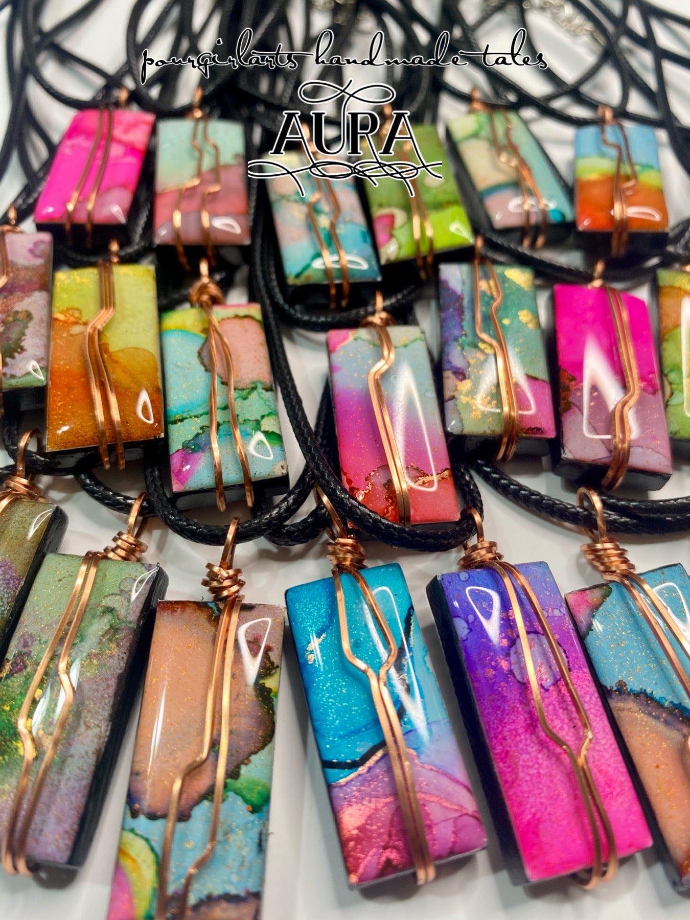 Colorful resin pendants with copper accents on black cords, branded 'Aura'.