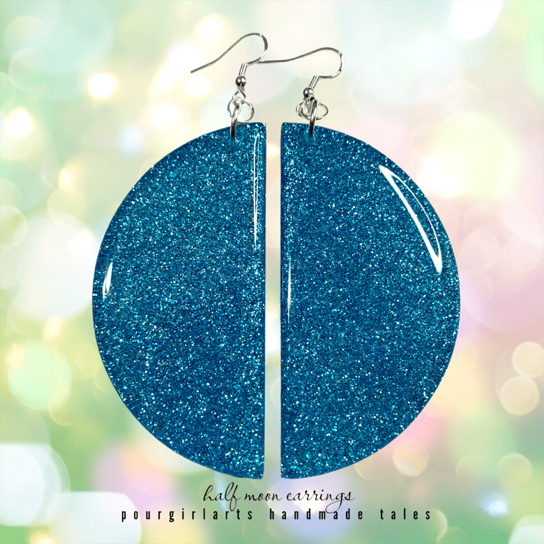 Blue glittery half-moon earrings on a blurred background with 'pourgirlarts' branding.