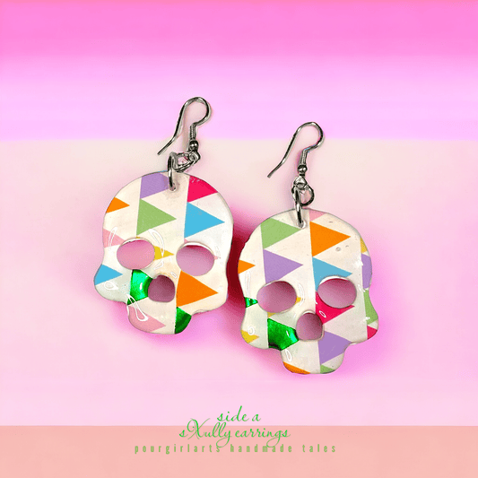 Colorful skull-shaped earrings on a pink background with 'side a' branding.