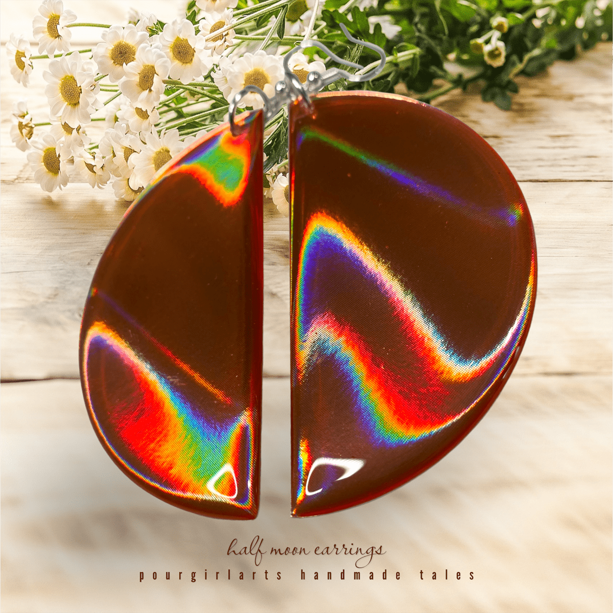 Half-moon earrings with rainbow iridescent finish on a wooden surface with flowers.