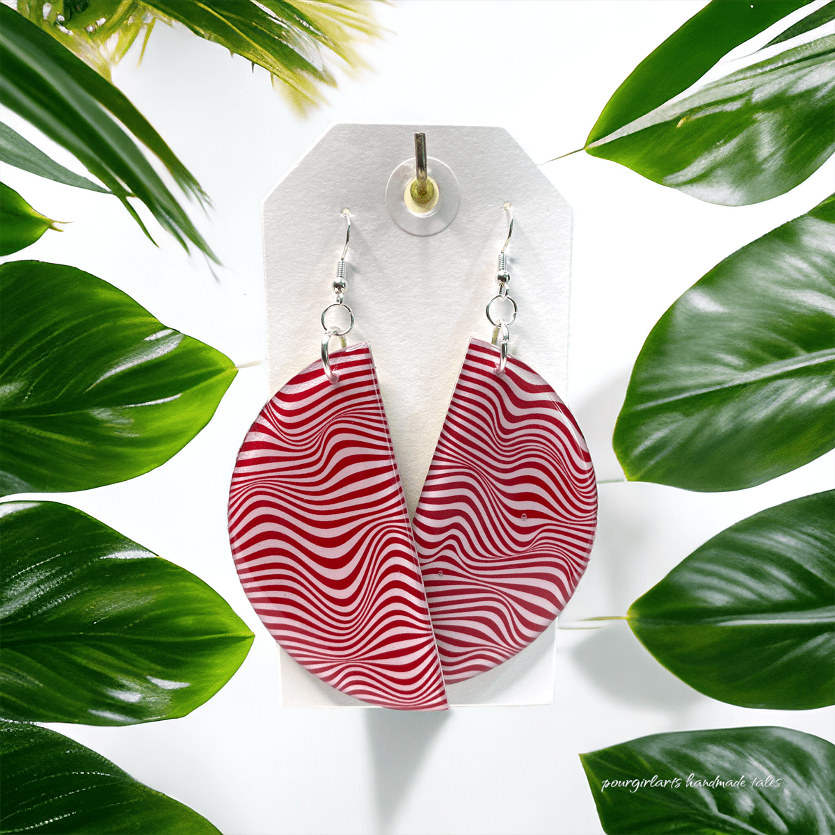 Red and white wavy patterned earrings on a white card with green leaves in the background