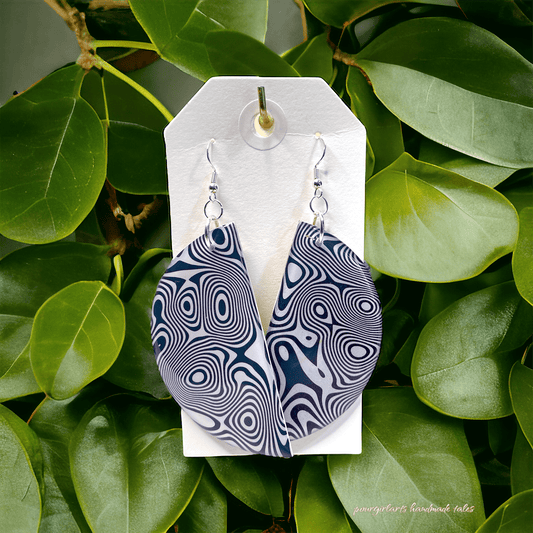 Pair of blue and white patterned earrings on a white card with green leaves in the background