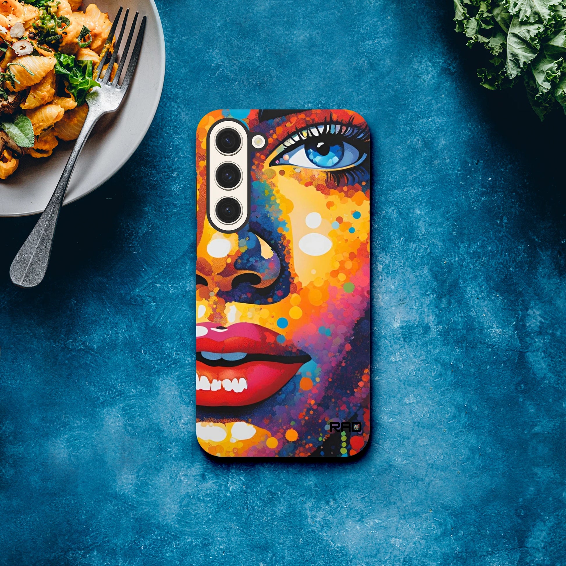 Colorful phone case with artistic design on a blue surface with food and greens.