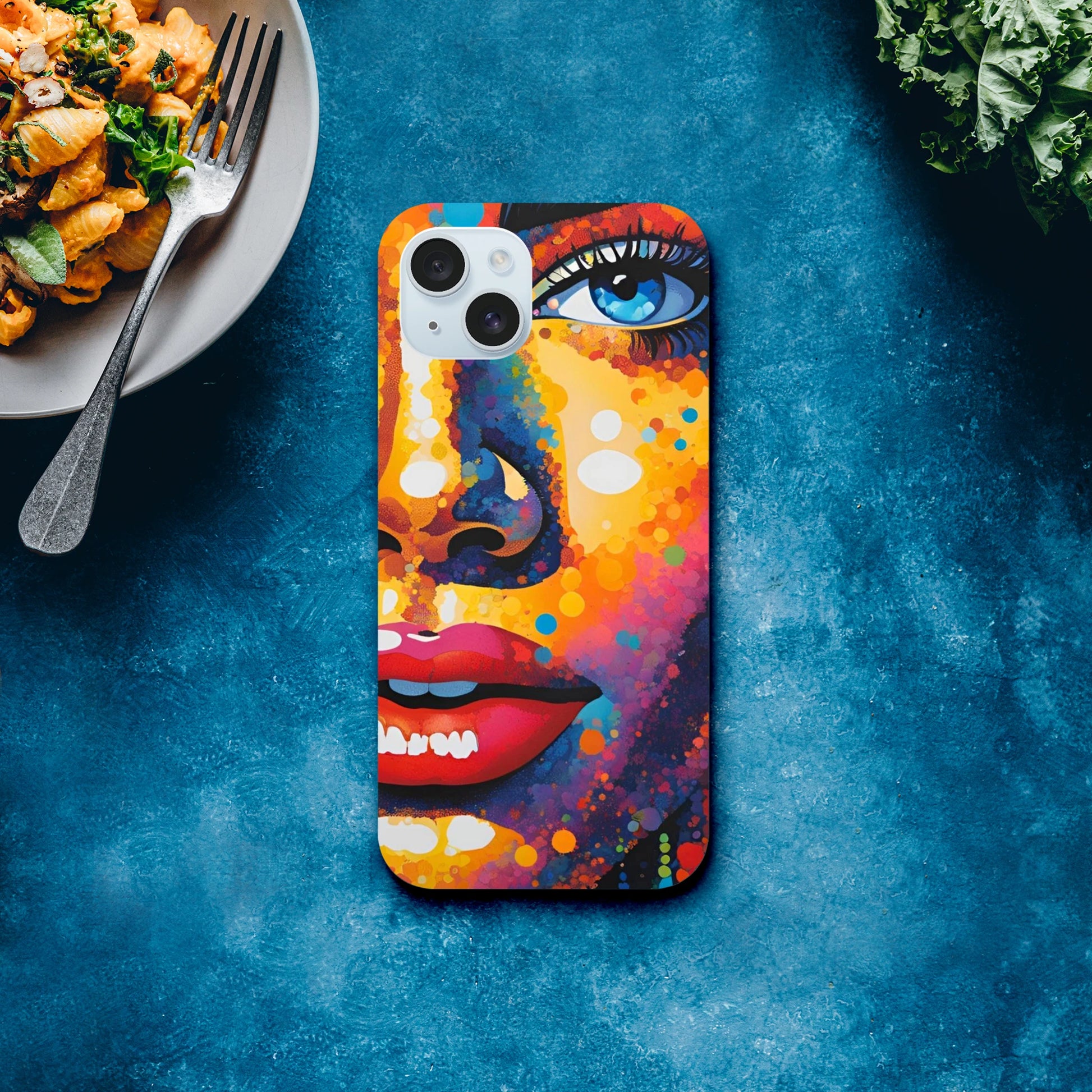 Colorful phone case with artistic design on a blue surface next to a plate of food.