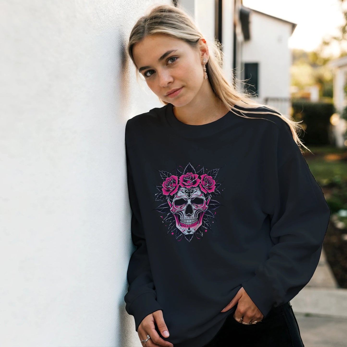 Woman wearing a black sweatshirt with a skull and roses design, standing against a light-colored wall.