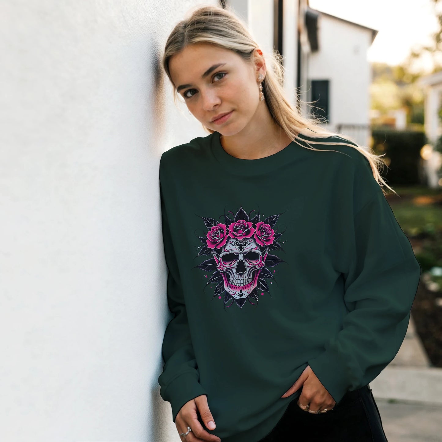 Woman wearing a dark green sweatshirt with a skull and floral design, standing against a light-colored wall.