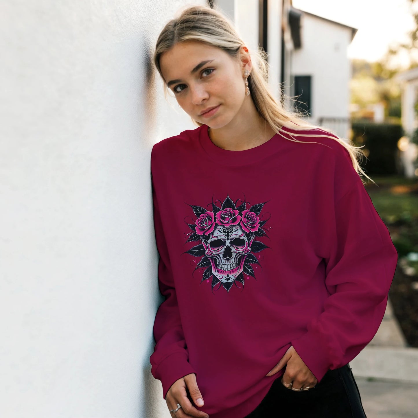 Woman wearing a maroon sweatshirt with a skull and floral design, standing against a light-colored wall.