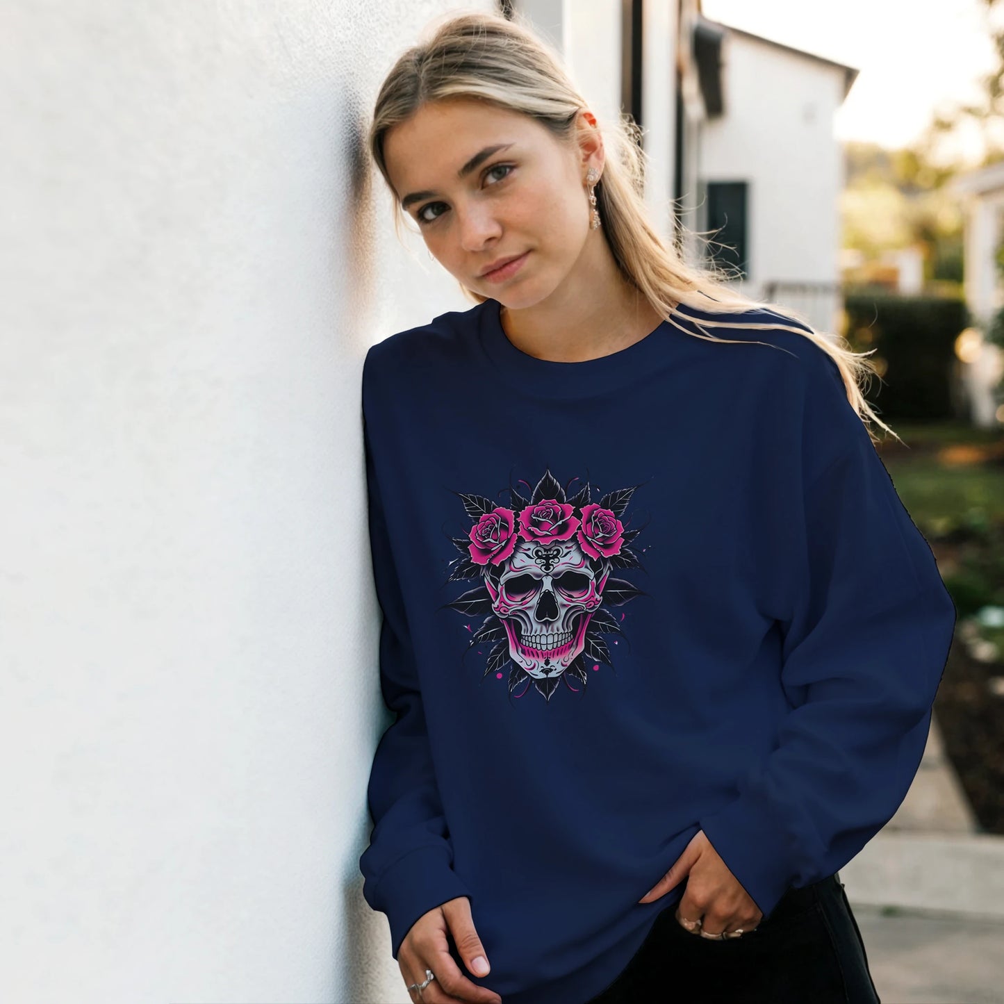 Woman wearing a navy blue sweatshirt with a skull and floral design, standing against a light-colored wall.