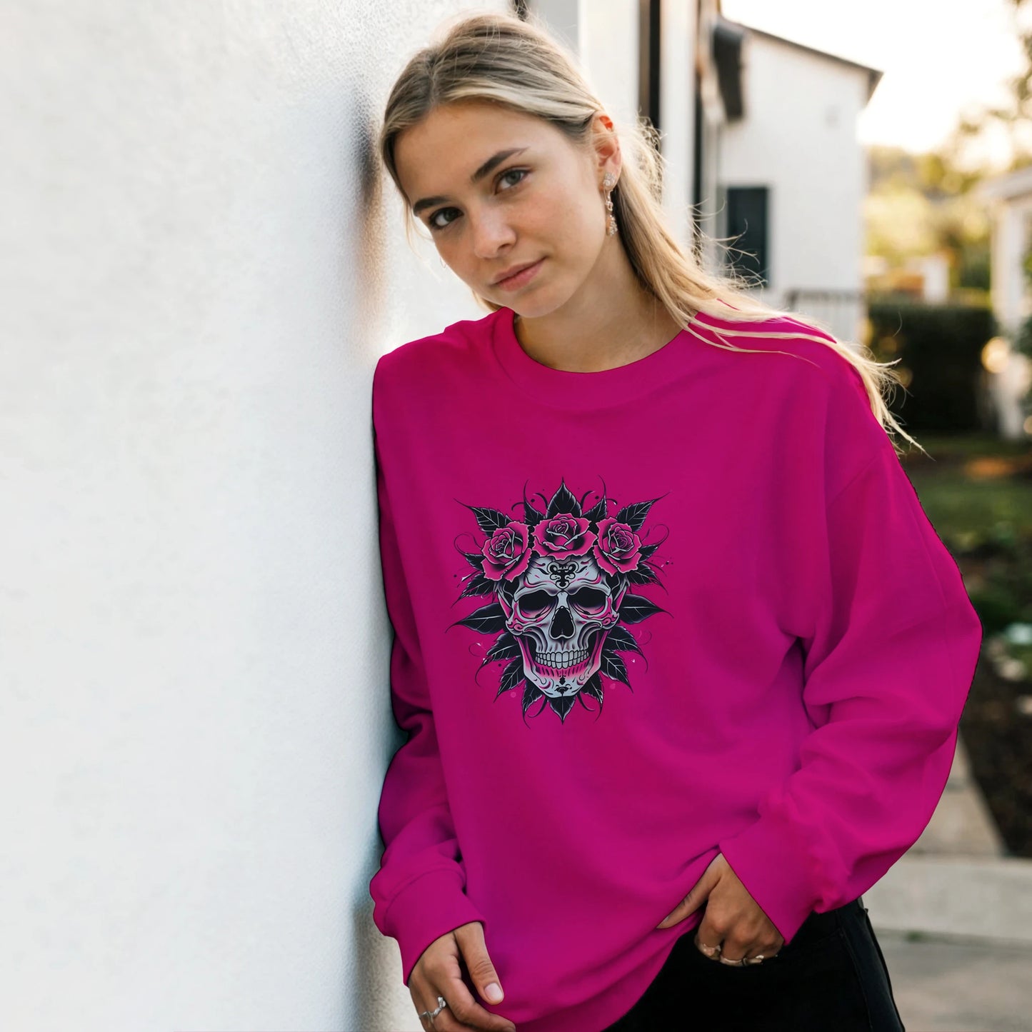 Woman wearing a pink sweatshirt with a skull and flower design, standing against a white wall.